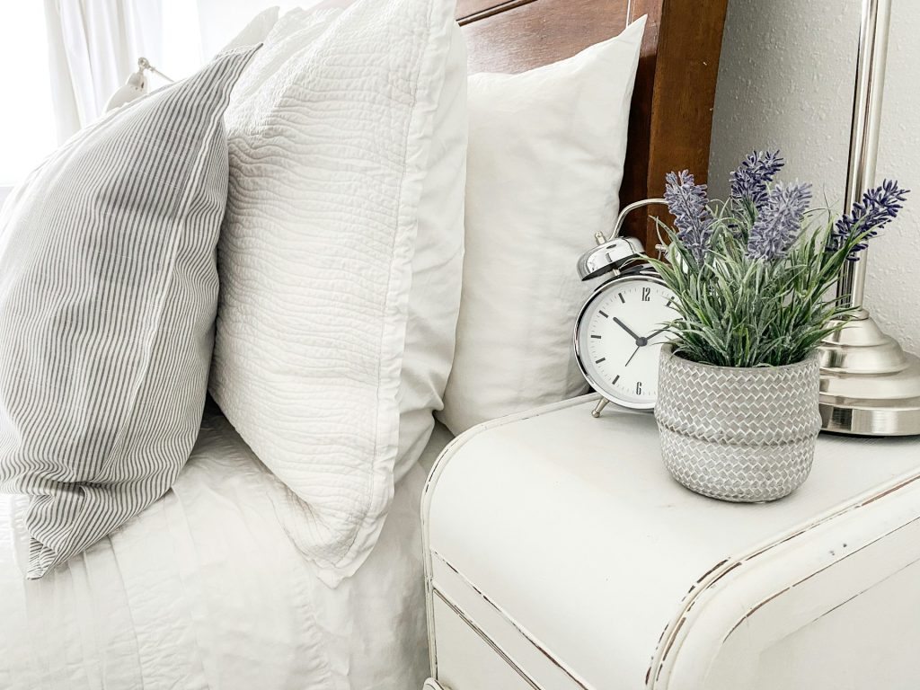 a cozy bed with an alarm clock and lavender plant - products for a better sleep